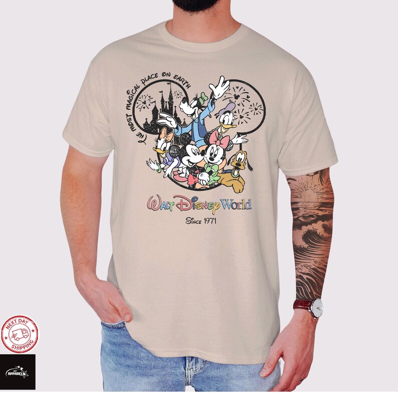 Puede incluir: Camiseta beige con un gr&aacute;fico colorido de personajes de Disney, incluyendo Mickey Mouse, Minnie Mouse y el Pato Donald. El dise&ntilde;o incluye el texto "Walt Disney World Since 1971" y "The Most Magical Place on Earth."