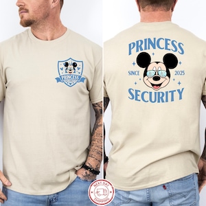 May include: Beige t-shirt featuring a Mickey Mouse graphic with the text "PRINCESS SECURITY" in blue. The front of the shirt has a shield design with the same graphic and text. The back of the shirt has the text "PRINCESS SECURITY" with the Mickey Mouse graphic.