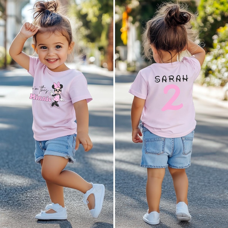 以下が含まれることがあります： 薄いピンク色のTシャツとデニムのショートパンツを着た幼い子供。Tシャツの前面にはミニーマウスのグラフィックと「I'm this Minnie」の文字があります。Tシャツの背面には「SARAH」という名前とピンク色の数字「2」があります。