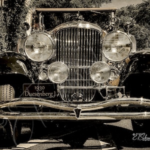 May include: A close-up view of a 1930 Duesenberg J, a classic car with a chrome grille and headlights. The car is black and has a chrome bumper.