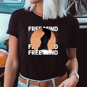 May include: Black t-shirt with a graphic of a silhouette of a person standing in front of an orange sun with the text "FREE MIND" repeated four times.