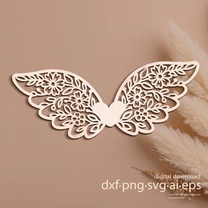 Puede incluir: Un diseño de alas de madera cortado con láser con detalles florales y de corazón. Las alas son de color marrón claro y tienen intrincados patrones recortados. La imagen incluye el texto "digital download dxf.png.svg.ai.eps".