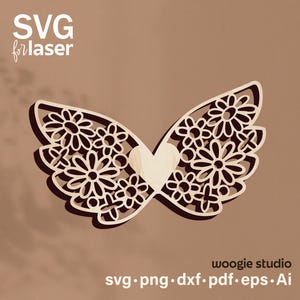 May include: A laser-cut wooden design featuring two symmetrical wings adorned with a floral pattern and a central heart shape. The text SVG for laser is in the top left corner, and the text woogie studio svg png dxf pdf eps ai is at the bottom.