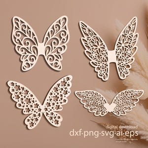 Puede incluir: Cuatro diseños de alas de mariposa de madera cortadas con láser. Cada juego de alas presenta patrones intrincados, incluyendo remolinos, flores y un corazón. Las alas se muestran sobre un fondo neutro, con el texto "digital download dxf.png.svg.ai.eps".