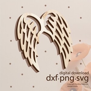 May include: A wooden cutout of angel wings in a light brown color. The wings are layered and have a delicate, intricate design. The image has a light brown background with small white dots.