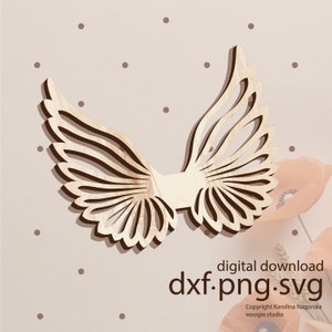 May include: A wooden cutout of a pair of angel wings with intricate details. The wings are light brown and have a delicate, layered design. The image includes the text "digital download dxf.png.svg Copyright Karolina Nagorska woogie.studio".