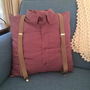 Peut inclure: Un oreiller à carreaux rouges et blancs avec des bretelles marrons attachées. L'oreiller est sur un canapé bleu.