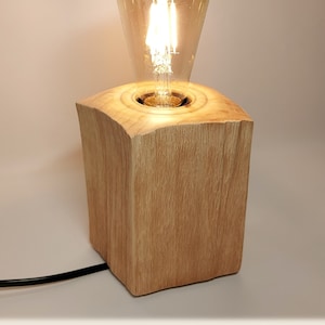 Könnte beinhalten: Eine Holztischlampe mit einer eingeschalteten Glühbirne. Die Lampe ist aus einem natürlichen Holzstamm gefertigt und hat ein schlichtes Design. Die Lampe ist eingesteckt und hat ein schwarzes Kabel.