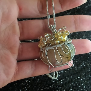 May include: A silver wire-wrapped pendant featuring a brown agate stone with a wire cage design. The pendant is adorned with small yellow beads.