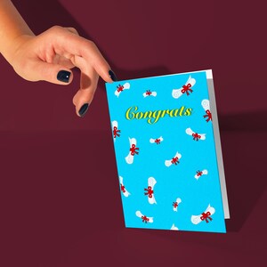 May include: A blue card with a white border and a pattern of white graduation caps with red bows. The card says "Congrats" in yellow letters.