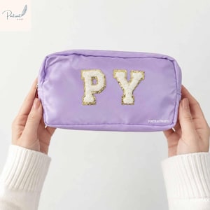 May include: A rectangular lavender pouch featuring two large, white, fuzzy varsity-style letters, P and Y, centred on the front. The letters have a gold glitter border. The word PORTRAITNGIFT is printed in small white text on the lower right side.
