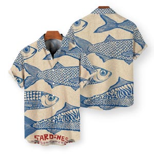 May include: A short-sleeved button-down shirt with a beige background and a repeating pattern of blue fish. The word "SARDINES" is printed in red at the bottom of the shirt. The shirt is displayed on a wooden hanger.