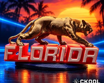 May include: A gold-colored panther figurine standing atop a red base with the white text FLORIDA embossed on the front. The panther is in a prowling stance with its mouth open, and the entire object is set against a vibrant sunset background.