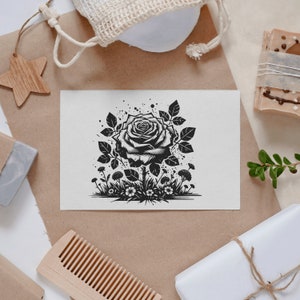 May include: A black and white illustration of a rose with leaves and small flowers surrounding it. The rose is in the center of the image and is the main focus.