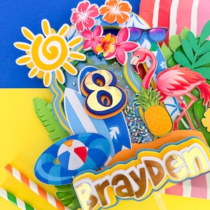 Puede incluir: Adorno de pastel colorido con temática de verano. Presenta un sol, flores, un flamenco, una piña, tablas de surf y un balón de playa. También incluye el nombre "Brayden" y el número "8".