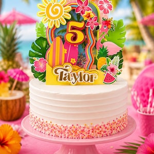 Può includere: Una torta con glassa bianca su un supporto rosa, sormontata da un colorato topper tropicale con il numero 5, il nome Taylor, un fenicottero rosa, tavole da surf, un sole giallo, fiori di ibisco, foglie di palma, un ananas e un'anguria.