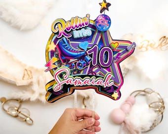 May include: A vibrant birthday cake topper with the words "Rollin' into 10 Samaiah". The design includes a roller skate, stars, and a disco ball. The topper is held by a clear stick.