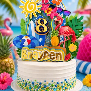 May include: A white frosted cake topped with a tropical-themed decoration featuring the number 8, the name Brayden, a yellow sun, a pink flamingo, a pineapple, a blue surfboard, a beach ball, and hibiscus flowers, all accented with colorful sprinkles.
