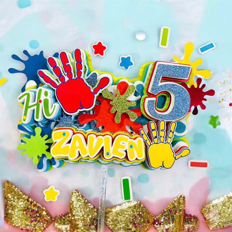 May include: A colorful cake topper with the name "ZAVIEN" and the number "5" in blue glitter. The topper also features handprints, paint splatters, and the word "Hi".