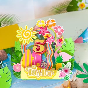 May include: A colorful birthday cake topper with a tropical theme. The design includes a large number 5, a flamingo, a surfboard, and the name "Taylor". The topper is decorated with flowers, a pineapple, and a watermelon slice.