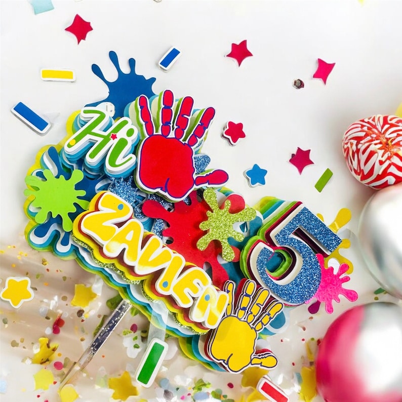 May include: Colorful cake topper with the name "Zavien" and the number "5" in blue glitter. The topper also features handprint shapes, paint splatters, and the word "Hi" in a bright, playful design.