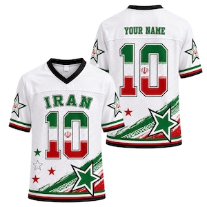 Puede incluir: Una camiseta blanca con cuello en V que muestra la palabra IRAN y el número 10 en verde y rojo con el emblema de la bandera iraní. El diseño incluye estrellas verdes y rojas, un cuello negro y un patrón de pincelada diagonal en el dobladillo.