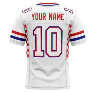 May include: White jersey with red and blue detailing. The number 10 is in large, bold, red and blue lettering. The text "YOUR NAME" is above the number. The sleeves have red and blue stripes.