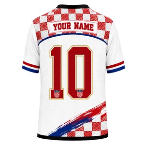 May include: A white short-sleeved jersey featuring a red and white checkered pattern on the shoulders and bottom hem. The back displays the text YOUR NAME above the large red number 10, which includes small checkered crests at the base.