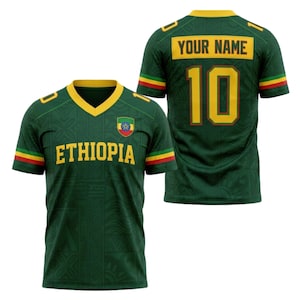 Puede incluir: Camiseta de fútbol verde con detalles amarillos, con la palabra "ETHIOPIA" en amarillo en el pecho. La camiseta tiene cuello en V y el número "10" en la espalda, con espacio para un nombre. Las mangas tienen rayas rojas, amarillas y verdes.