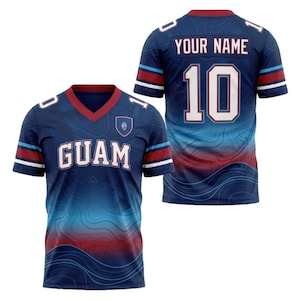 May include: A dark blue V-neck jersey featuring the word GUAM in white letters on the front, a small Guam seal emblem, and a topographic map pattern. The back displays the number 10 and the text YOUR NAME in white with a red collar and sleeve trim.
