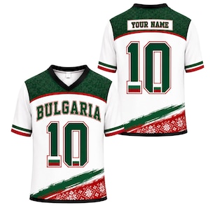 May include: A white V-neck jersey featuring the text BULGARIA and the number 10 in green with red outlines. The design includes dark green textured shoulders, a red and green diagonal stripe, and a red snowflake pattern at the bottom hem.