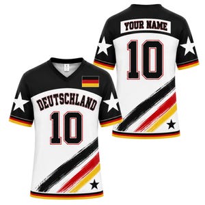 Op de afbeelding: Een shirt met korte mouwen en V-hals in een zwart-wit kleurenschema met de Duitse vlag, het woord DEUTSCHLAND en het nummer 10 op de voorzijde. De achterzijde toont de tekst YOUR NAME en het nummer 10, met diagonale strepen in zwart, rood en goud.