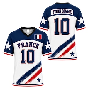May include: A V-neck sports jersey featuring a white and navy blue color scheme with red accents. The front displays the text FRANCE, the number 10, and a French flag. The back shows the text YOUR NAME and the number 10. Both sides feature star graphics.
