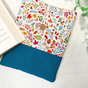 May include: A teal blue book cover with a white fabric insert featuring a colourful autumn leaf pattern. The fabric has a variety of leaves, flowers, and acorns.