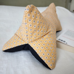 May include: A yellow and white patterned pillow with a black trim. The pillow is shaped like a long, narrow triangle.