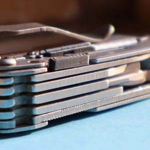 May include: Close-up of a silver multi-tool. The tool has a bottle opener, knife blades, and other implements. The tool is partially open, revealing its layered construction and intricate design. The tool is made of metal.
