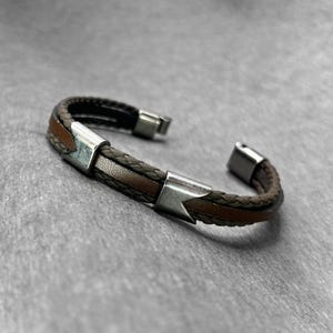 May include: A brown leather bracelet with silver accents. The bracelet is braided and has a simple design.