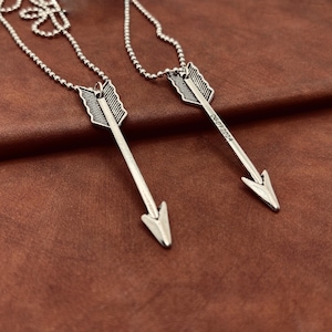 Op de afbeelding: Twee zilveren pijlkettingen met een bolketting. De pijl hanger aan de linkerkant heeft een gedetailleerd ontwerp en de pijl hanger aan de rechterkant heeft de datum 06.07.2024 gegraveerd.