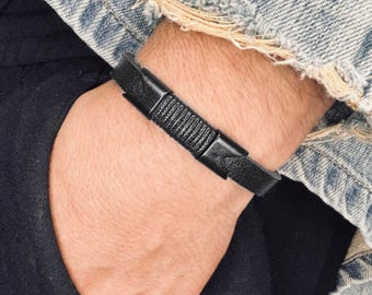 May include: A black leather bracelet with a braided design and a silver buckle.