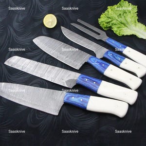 May include: A set of five kitchen knives with stainless steel blades and white and blue handles. The blades have a unique pattern. The handles are white with blue accents. The text "Saasknife" is visible in the image.