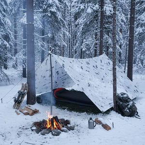 Op de afbeelding: Een winterkampeerscène in een besneeuwd bos. Een witte zeildoekschuilplaats is opgezet met een slaapzak erin. Een kampvuur brandt voor de schuilplaats, met sneeuwschoenen en een rugzak in de buurt. De bomen zijn bedekt met sneeuw.