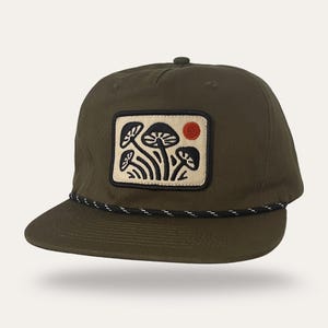 May include: Olive green baseball cap with a flat brim and a black and white rope detail. The cap features a rectangular patch with a mushroom design and a red sun. The cap is a stylish accessory.