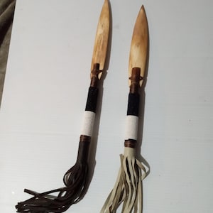 May include: Two handmade bone knives with leather tassels. The knives have black and white beaded wrappings. One knife has a brown tassel and the other has a white tassel.