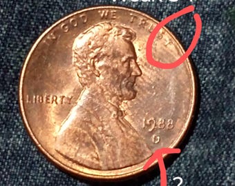 Op de afbeelding: Een koperkleurige Lincoln-munt uit 1988 met de tekst "IN GOD WE TRUST" en "LIBERTY". De munt heeft de tekst "Weak ST" en een vraagteken op de afbeelding.