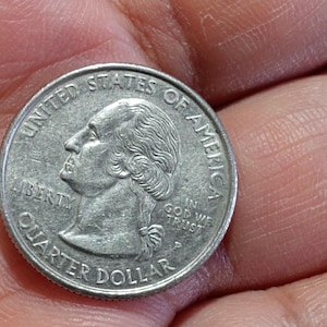 May include: A United States quarter dollar coin, featuring a profile of George Washington, the words "LIBERTY", "QUARTER DOLLAR", and "IN GOD WE TRUST". The coin is silver in color.