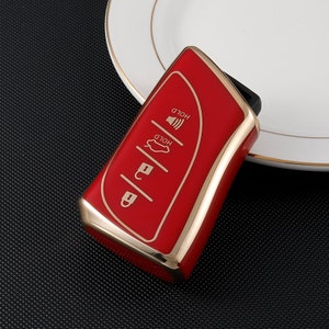 May include: Red car key fob with gold trim and four buttons. The buttons are labeled "HOLD" and have icons for a car, a lock, and a speaker.