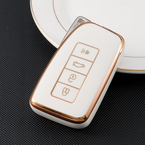May include: White car key fob with a rose gold trim. The key fob has four buttons: unlock, lock, trunk, and panic.
