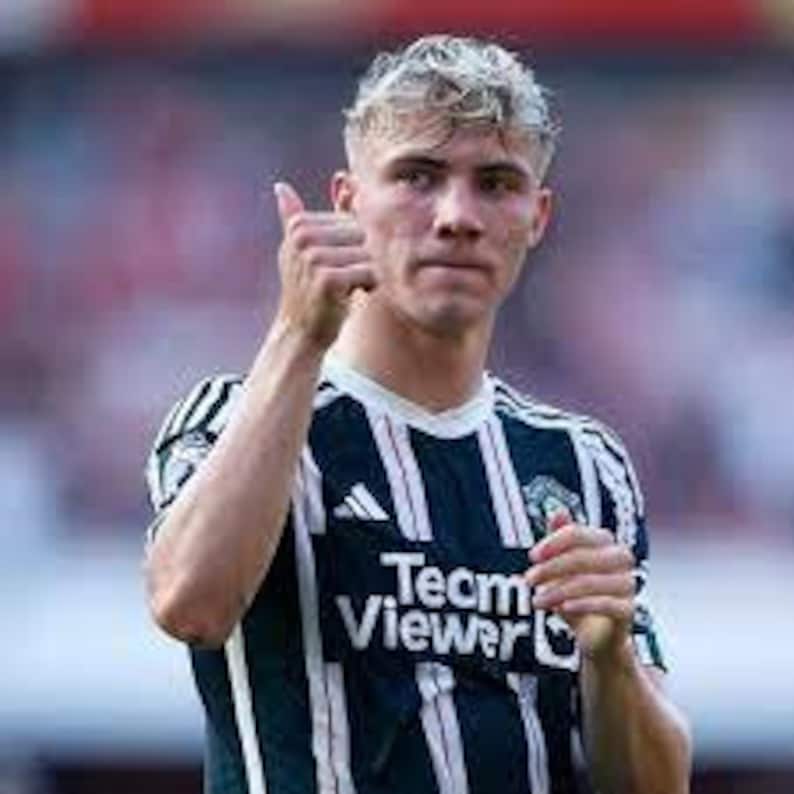 May include: A young man wearing a white and black striped football shirt with the text "TeamViewer" on the front. He is giving a thumbs up.