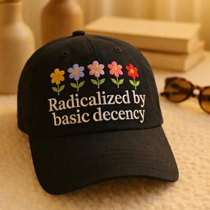May include: Black baseball cap with embroidered flowers in yellow, purple, pink, and red. The cap features the phrase "Radicalized by basic decency" in white lettering. A stylish accessory for everyday wear.