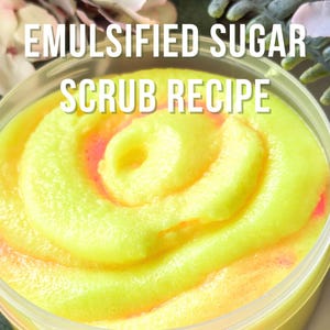 May include: A clear plastic container filled with a vibrant yellow and pink emulsified sugar scrub. The scrub is swirled in a spiral pattern. Text on the image reads "EMULSIFIED SUGAR SCRUB RECIPE" and "A STEP-BY-STEP GUIDE FOR NEW AND EXPERIENCED FORMULATORS."